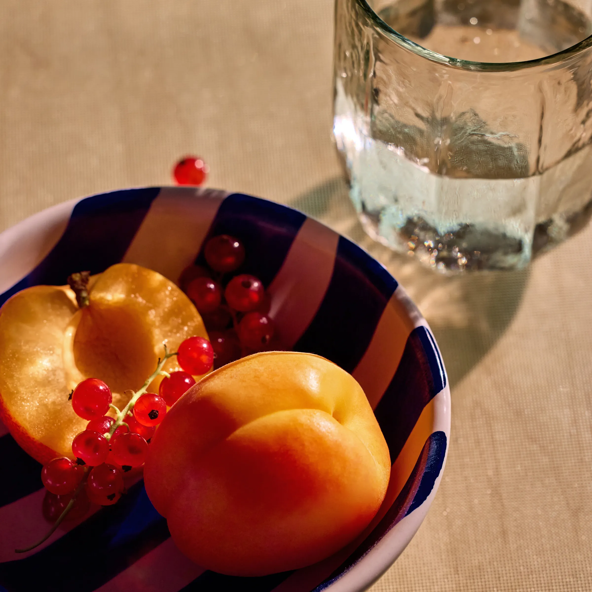 Apricots and currants in a striped bowl beside a glass of water